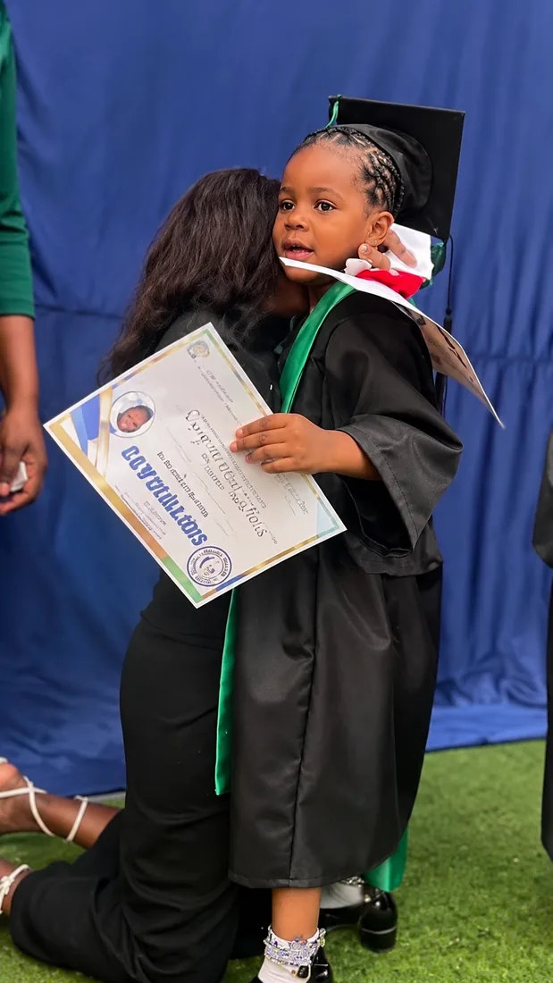 Une enfant diplômée serrée dans les bras, son certificat à la main